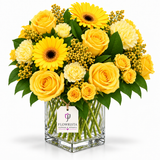 A vibrant yellow floral arrangement featuring yellow roses, sunflowers, and cream carnations in a clear glass vase with a visible Flowrista tag, set against a clean white background.