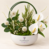 Artificial white anthuriums and globe-shaped blooms with green loops in a white Flowrista bowl