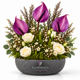 Artificial purple anthuriums and white roses with decorative foliage in a grey oval Flowrista bowl