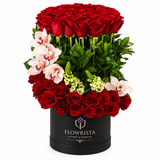 Tiered red roses pale pink orchids and greenery in a black round Flowrista flower box
