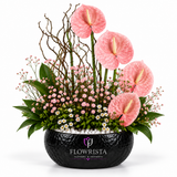 Artificial pink anthurium flower arrangement with white pebbles and greenery in a black Flowrista bowl
