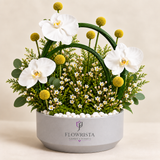 Artificial white orchids and yellow ball flowers with green loops in a grey Flowrista pot