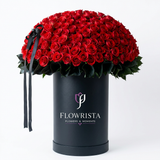 Full round red rose arrangement with green foliage in a tall black Flowrista box and black ribbon