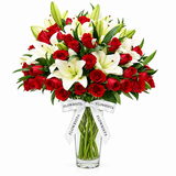 Flowrista red roses and white lilies with green buds in a clear glass vase with a white ribbon