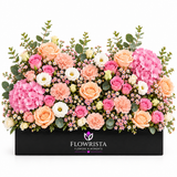 Fresh pink hydrangeas peach and pink roses carnations and white lisianthus in a black rectangular Flowrista planter