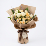 Fresh white and peach roses with peach spray roses and greenery in brown paper wrapping with Flowrista ribbon