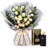 Amir Al Oud Black Intense perfume and box beside a cream rose and pale-blue flower bouquet