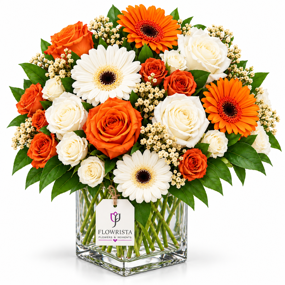 A vibrant floral arrangement in a clear square glass vase, featuring orange and white roses, orange and white gerbera daisies, and green foliage, with a 'FLOWRISTA' tag on the vase, set against a solid white background.