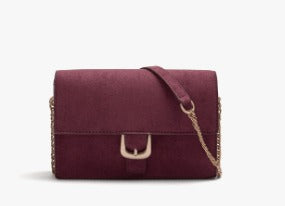A burgundy suede crossbody handbag with a gold-tone buckle and chain strap, shown against a plain white background.
