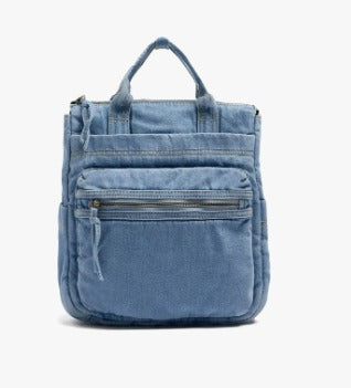 A light blue denim backpack with top handles and a front zippered pocket, shown against a plain white background.