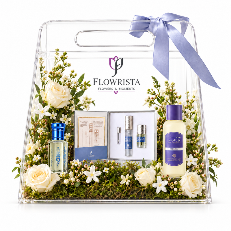 A clear acrylic gift bag filled with floral arrangements, green moss, and several Flowrista-branded toiletry or fragrance items, tied with a lavender ribbon, on a white background.