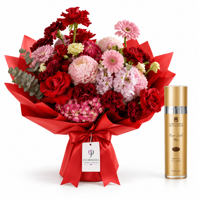 A vibrant flower bouquet with red, pink, and white flowers wrapped in red paper with a tag from 'Flourisha', next to a gold bottle of 'Rose Gold Mist' on a white background.