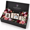 A luxury gift set from Flowrista Flowers & Moments in an open black box, decorated with pink, red, and purple roses and green eucalyptus leaves, containing skincare and cosmetic products.