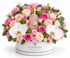 A luxury floral gift arrangement featuring a pink Chanel No. 5 perfume bottle nestled in a vibrant bouquet of pink and peach roses, white orchids, and green foliage, presented in a white round box branded FLOWWRISTA.