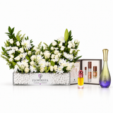 A floral arrangement in a rectangular glass planter with white flowers and green foliage, displayed alongside perfume bottles and a branded Flowerista box on a clean white background.