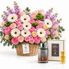 A floral gift arrangement in a wicker basket with pink and white flowers, shown with a perfume bottle, a boxed fragrance set, and a small gold perfume vial on a clean white background. A hanging tag reads FLOWFLOWER.