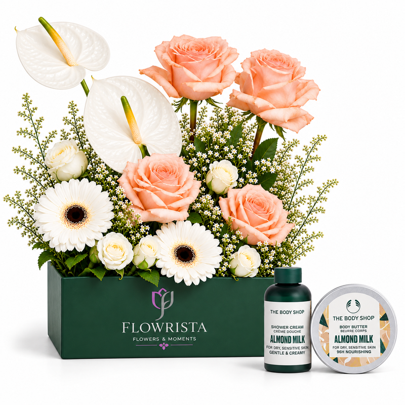 A floral gift arrangement in a dark green rectangular box from Flowrista, featuring peach roses, white anthuriums, white gerbera daisies, and green foliage, styled with a small bottle and round tin from The Body Shop on a white background.