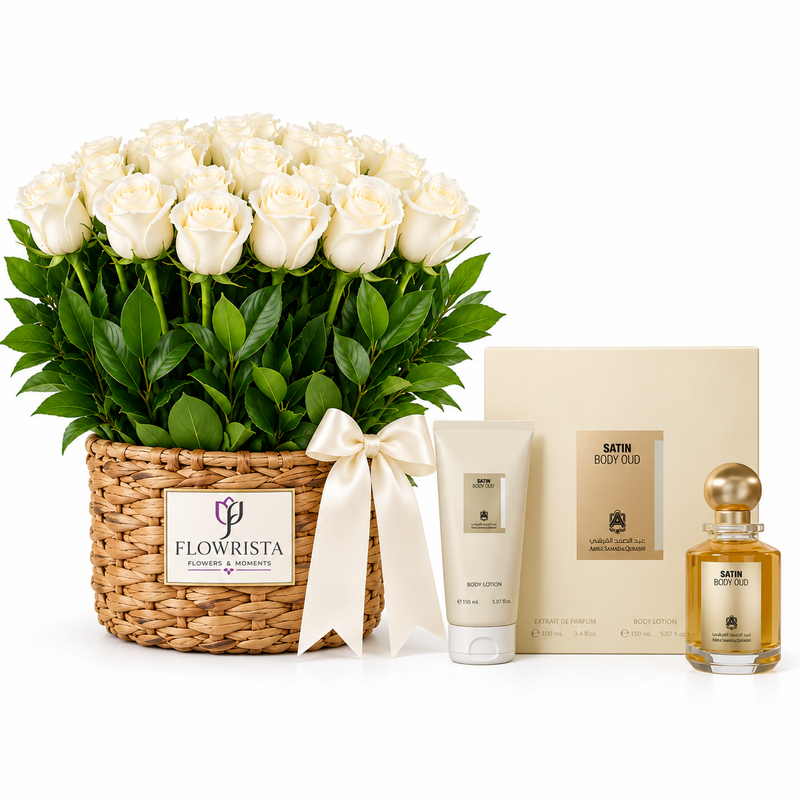 A luxury gift set featuring a large basket of white roses with green leaves, a woven basket, a cream satin body oil box, a white body lotion tube, and a small satin body oil bottle with a gold cap on a white background.