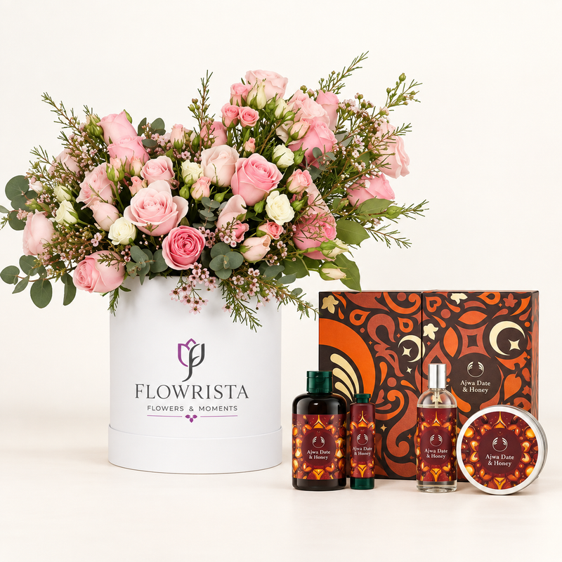 A curated gift set featuring a large pink and white flower arrangement in a white cylindrical container labeled 'FLOWRISTA', alongside matching home fragrance products including two dark bottles, a clear spray bottle, and a round tin with patterned labels, all arranged on a clean white background.