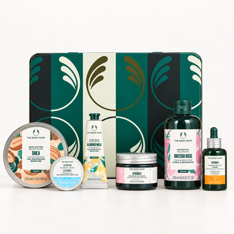 The Body Shop Bath & Body Set featuring a green and cream patterned gift tin with six bath products arranged in front on a white background: Shea butter, Almond Milk hand wash, British Rose shower gel, Hydrate body wash, and two Vitamin dropper bottles.