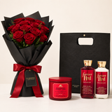 A Valentine's Day gift set featuring a bouquet of 24 red roses in black wrapping with a red ribbon, a Bath & Body Works 'Forever Red' body wash bottle, a body lotion bottle, and a Strawberry Punch bath bomb jar, alongside a black gift bag.