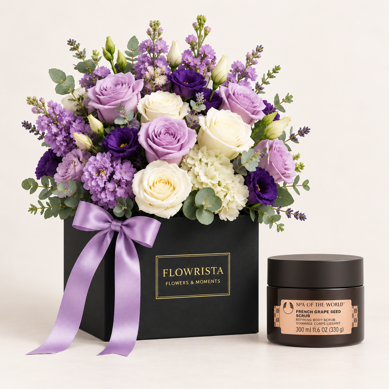 A luxury gift set featuring a black box of 'Flowrista' flowers and moments with a purple satin ribbon, next to a jar of 'Sapna' French Grape Seed Scrub, set against a clean off-white background.