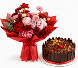 A red and pink flower bouquet wrapped in red paper with a red ribbon, placed beside a chocolate cake with chocolate shavings and a red ribbon on a white background.