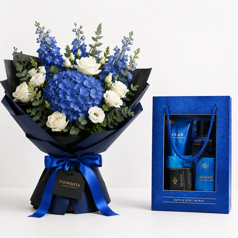 A floral bouquet with blue hydrangeas, blue delphiniums, white roses, and green eucalyptus wrapped in dark blue paper with a blue ribbon, shown beside a blue gift box containing bath and body items labeled Ocean and Flowwrista.
