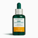 The Body Shop Vitamin C Glow Revealing Serum in a dark green glass dropper bottle with a white and orange label, set against a clean white background.