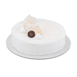 A round white cake with textured frosting, decorated with white meringues, cream swirled pastries, and a chocolate truffle, presented on a silver cake board against a white background.