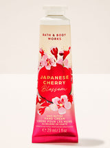 A squeeze tube of Bath & Body Works Japanese Cherry Blossom Shea Butter Hand Cream, featuring a cream and pink gradient background with red cherry blossom illustrations and a large red oval label.