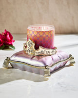 Decorative candle with a crown on a pink cushion against a neutral background