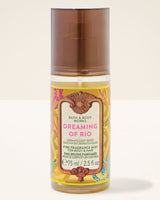 A bottle of Bath & Body Works Dreaming of Rio Fine Fragrance Mist for body and hair, featuring a translucent brown cap and a colorful yellow label with pink and brown accents, set against a plain off-white background.