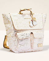 A light pink and gold patterned backpack with gold-tone hardware, featuring a top handle, a hanging keychain charm, and front pockets, photographed on a clean off-white background.
