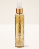 A bottle of Disney's Life as a Fairytale Bath & Body Works shower spray, featuring a gold cap, clear spray nozzle, and a gold-tinted liquid with gold glitter and multicolor fairy tale illustrations, set against a plain off-white background.