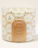 A three-wick Disney Princess 'Life's a Fairytale' soy wax blend candle in a clear glass jar with a white label decorated with gold chain motifs and small pastel fairy tale illustrations. The label features the Disney Princess logo and product details.