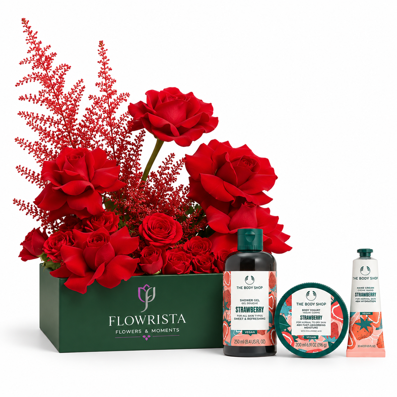 A curated gift set featuring a large bouquet of red roses and red berries in a dark green box labeled Flowrista, alongside three The Body Shop Strawberry themed products: shower gel, hand cream, and a scrub in a white tube.