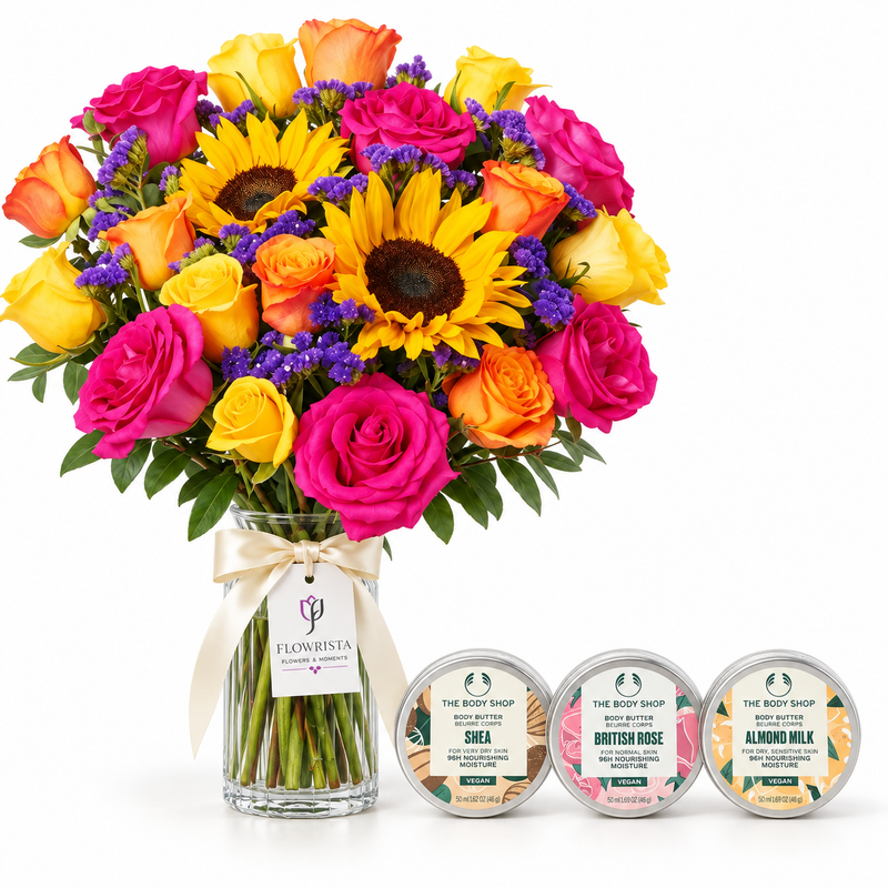A vibrant flower bouquet in a clear glass vase with a cream ribbon and tag, paired with three round body care gift boxes from The Body Shop on a white background.