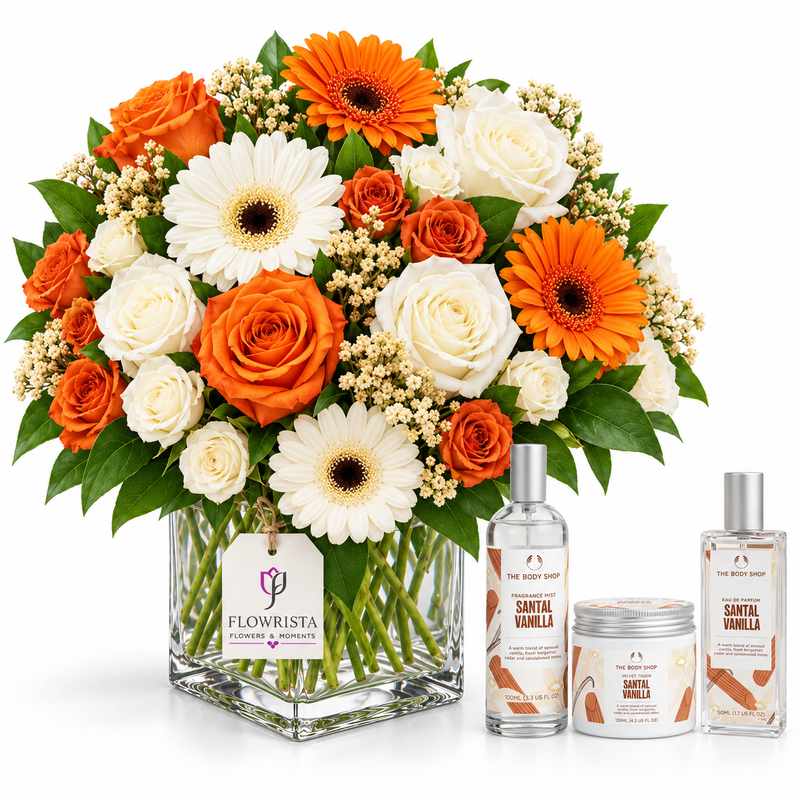 A floral arrangement in a clear square glass vase with orange gerbera daisies, white roses, orange roses, and green foliage, displayed beside three matching Flowrista Santa Vanilla scented products on a white background.