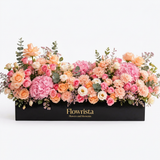 Pastel pink hydrangeas, peach roses and mixed flowers with greenery in a long black Flowrista box