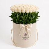 White roses and green foliage in a tall cream Flowrista hatbox with ivory satin bow and ribbon handles
