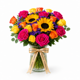 Flowrista sunflowers and pink, orange and yellow roses in a clear glass vase on a white background