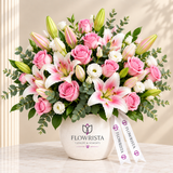 Pink roses, pink lilies and white lisianthus in a white Flowrista pot with ribbon