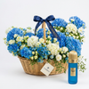 Brazilian Tobacco 100 ml perfume beside a Flowrista basket of blue and white hydrangeas, white roses and carnations
