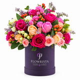 Magenta pink peach and cream roses with orange berries in a purple Flowrista round box