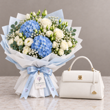 White Call It Spring top-handle bag beside Flowrista blue hydrangea and white rose bouquet